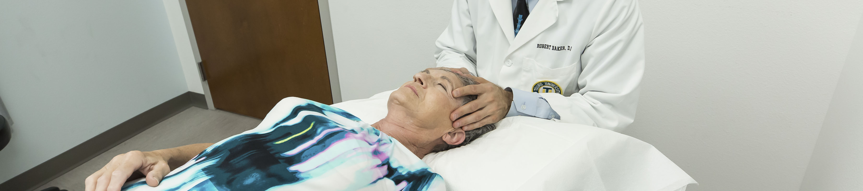 A patient lays on an exam table in a doctors office while a physician examines their temples