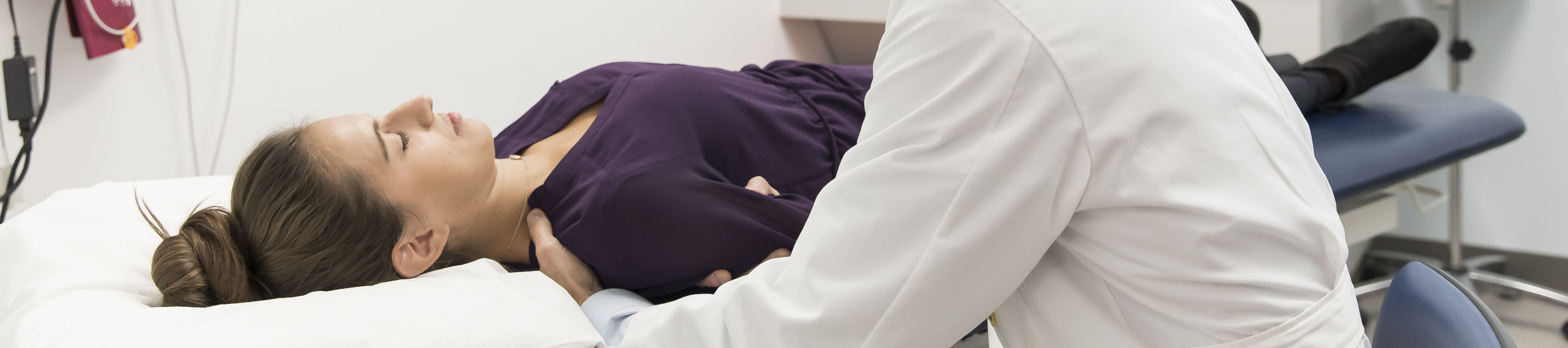 A patient lays on an exam table in a doctors office while a physician examines their arm and shoulder